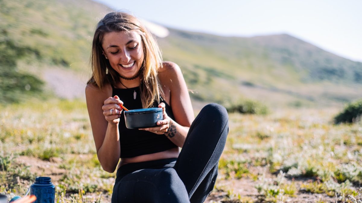 woman in black tank top and black pants sitting on ground holding blue ceramic mug during